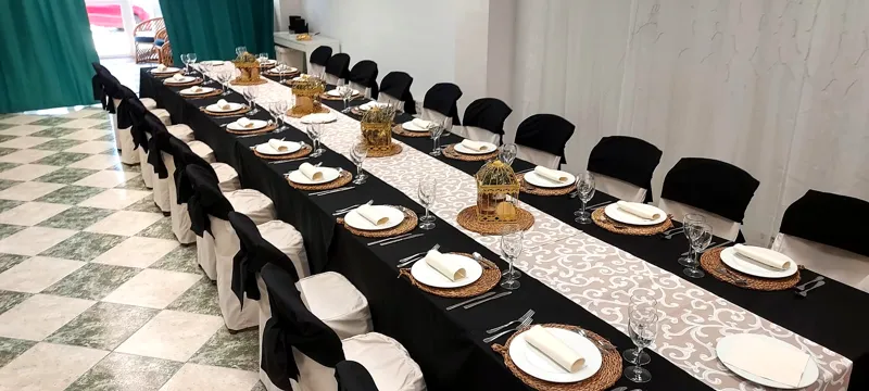 Mesa corrida elegante con copas, centros de mesa y sillas negras en la sala de Lacasa
