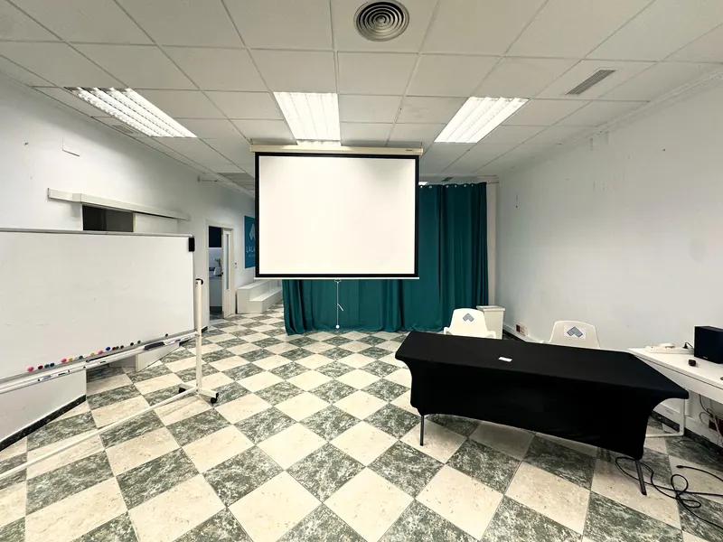 Pantalla de proyector, pizarra blanca y mesa negra frente a las cortinas verdes
