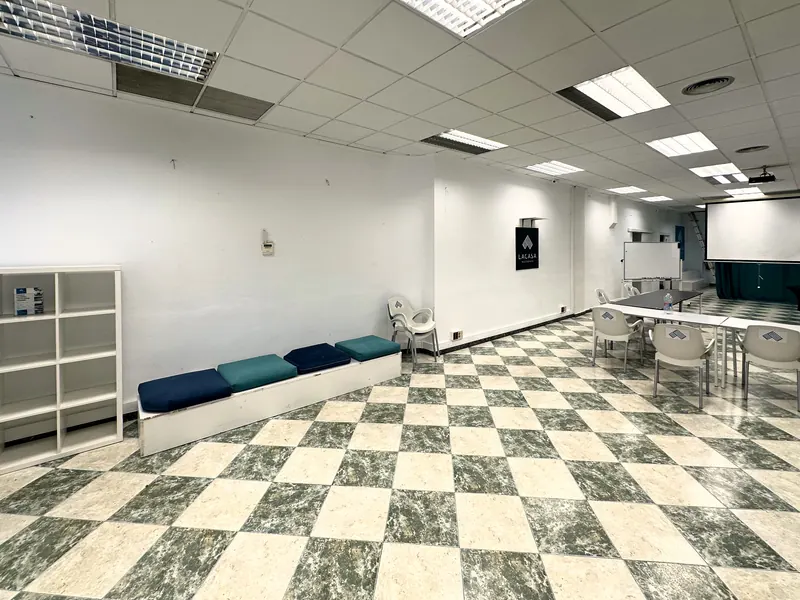 Vista general de la sala con banco de cojines, estantería y mesas al fondo